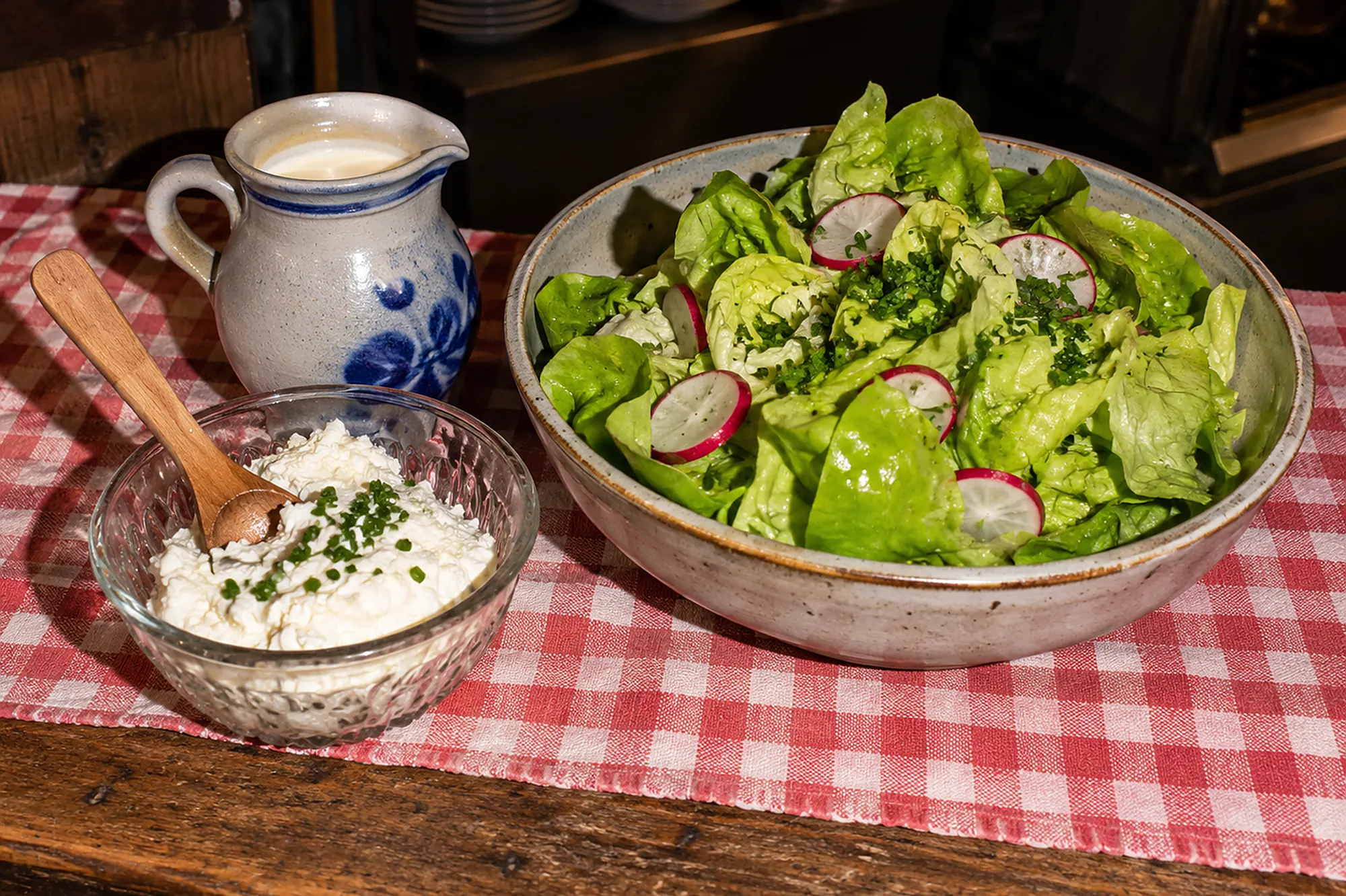 Schüssel mit grünem Kopfsalat, Radieschen und Schnittlauch, daneben ein Krug Rahm und ein Schälchen Quark